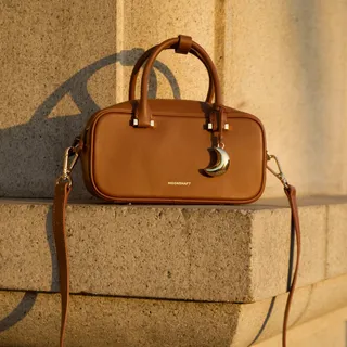 The Crescent Bowling Bag in Cognac. A warm, composed, and quietly striking color. Crafted from supple nappa leather with a structured, elongated silhouette and a flat base that stays upright. Twin zip